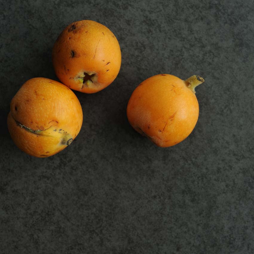 Drei orange Mispeln auf dunkler Platte