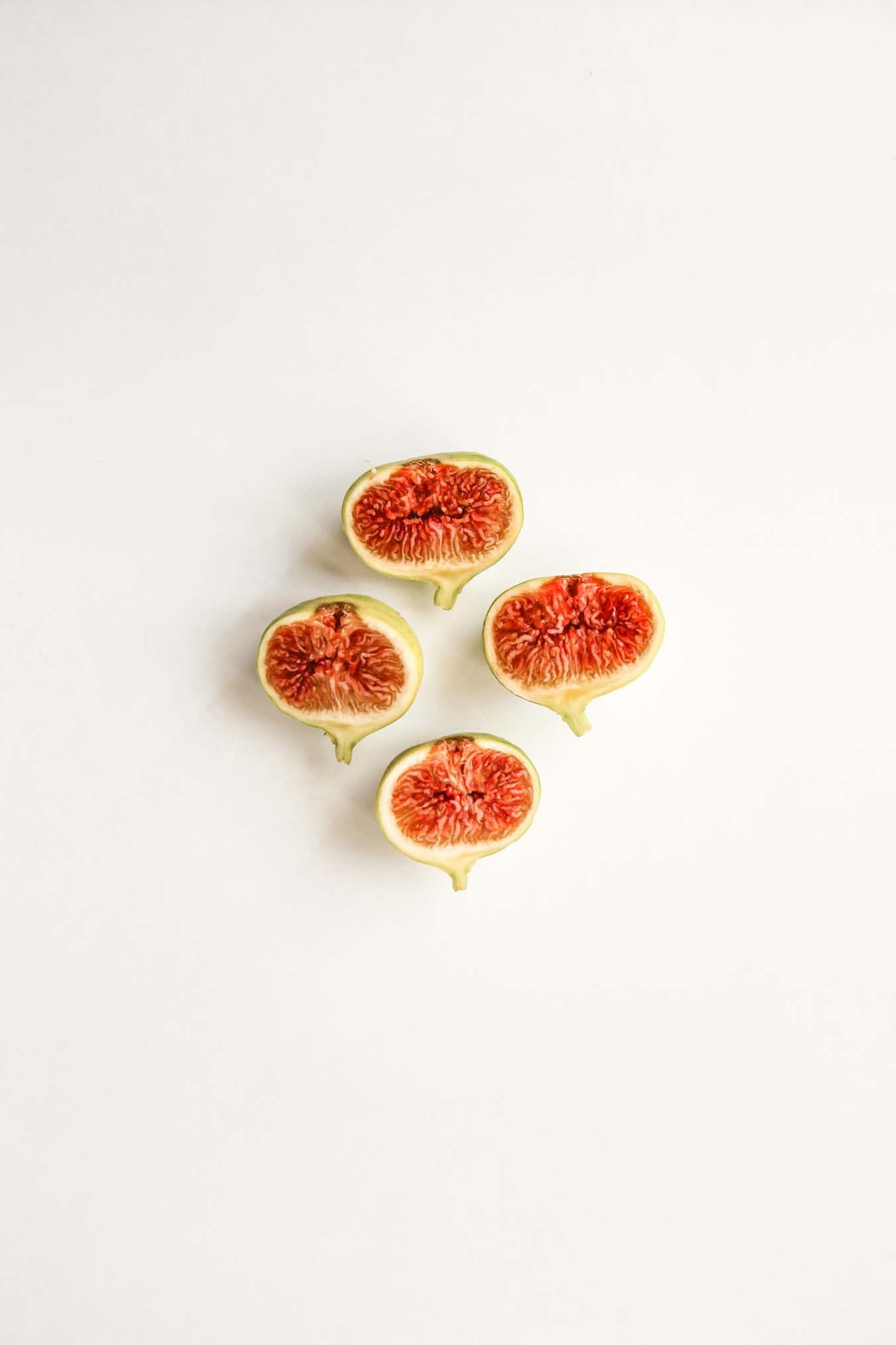 four red fleshed fig halves are lying on a white background - their stem bases point downward