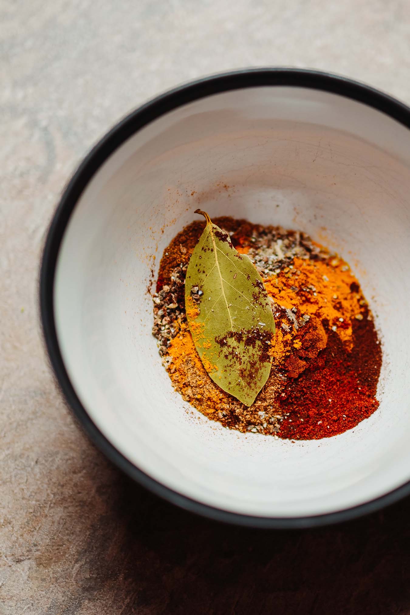 red and orange spices and a bayleaf in a bowl