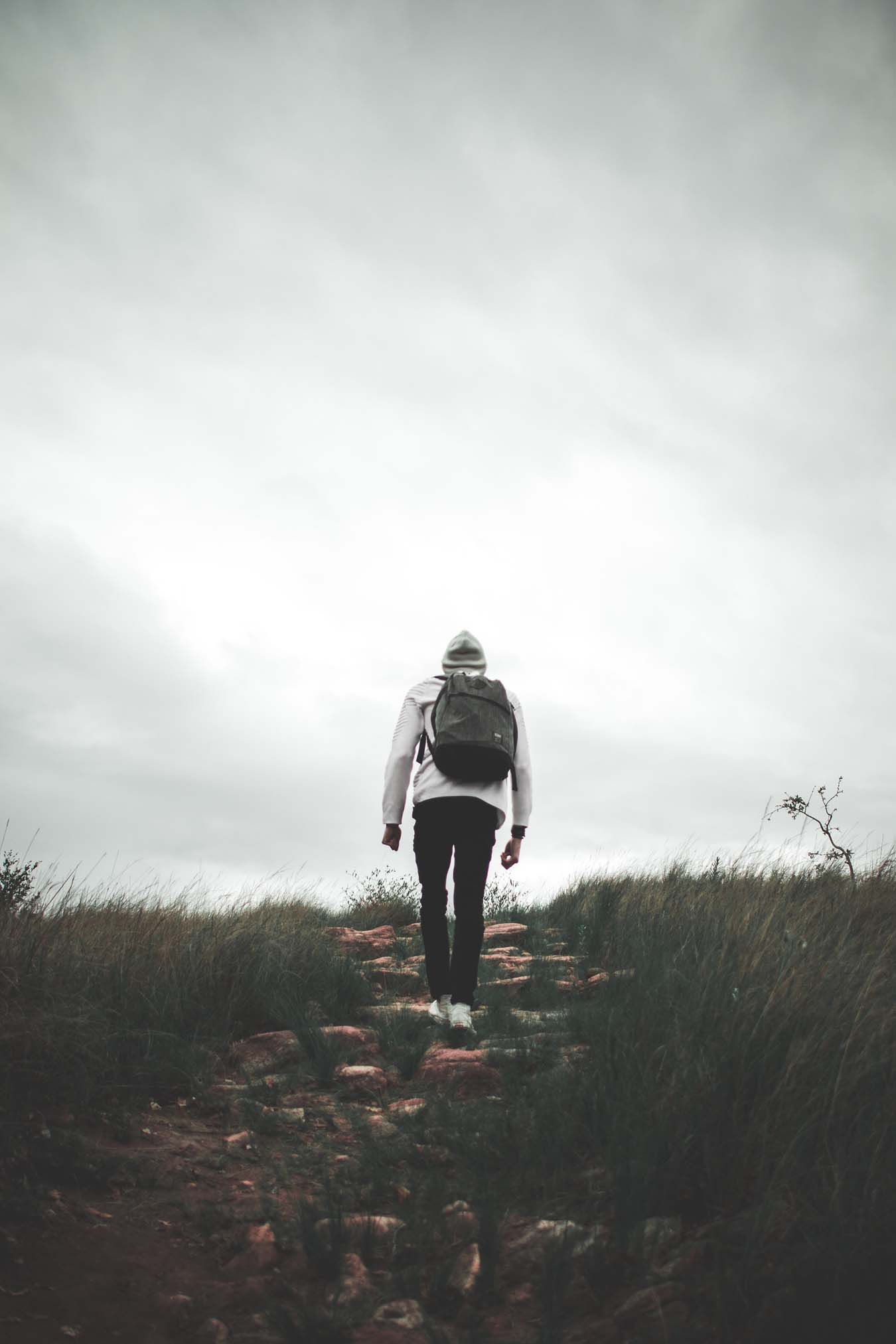 A person with a backpack and a hood is walking up a stony path.