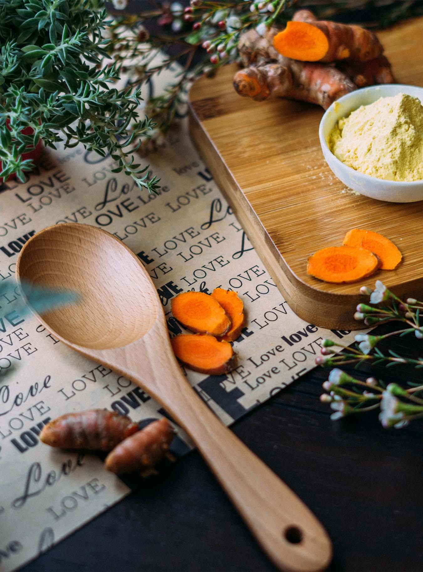 Yellow tumeric powder, a fresh tumeric root and some spices on a wooden board.