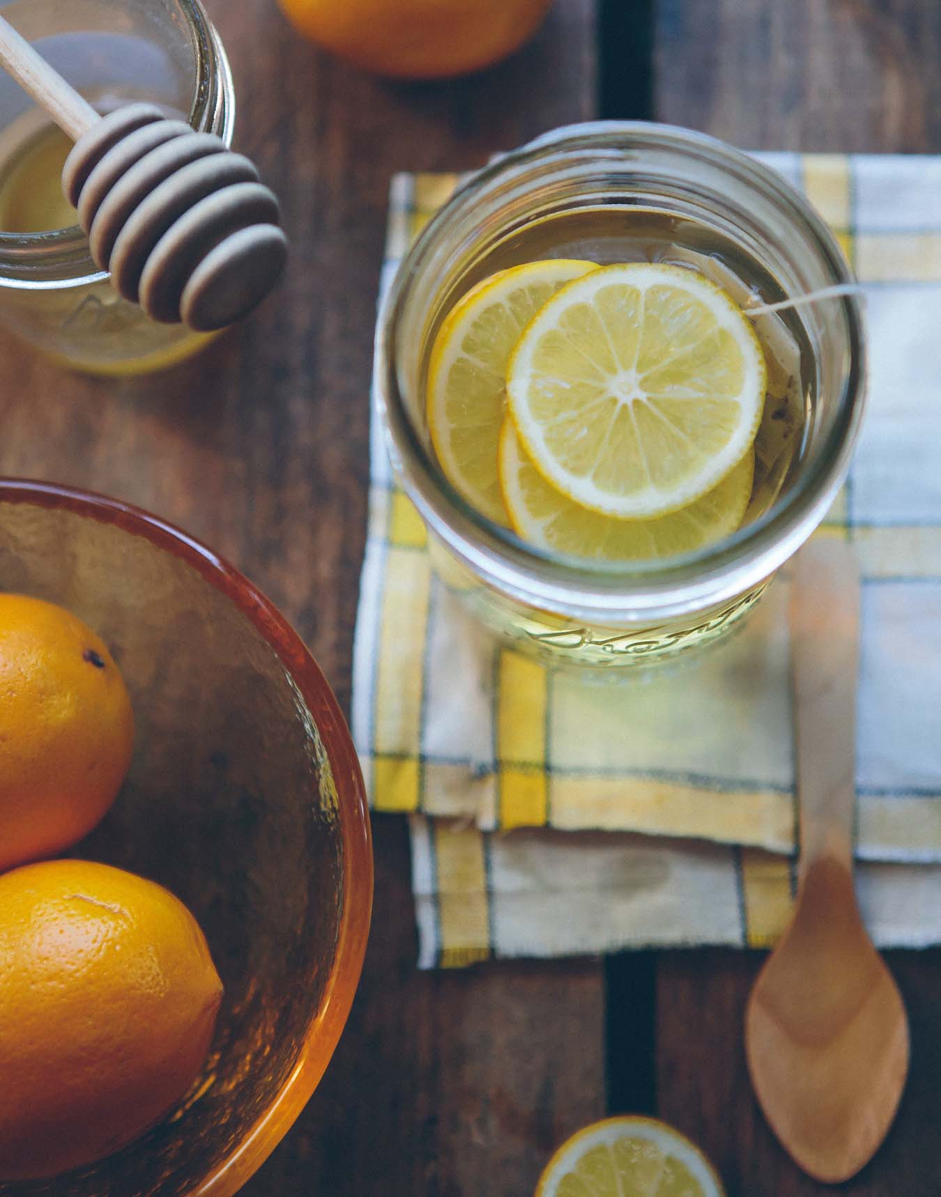 Lemon tea in a glass mug stands on a cloth - honey jar and orange citrus fruits next to it