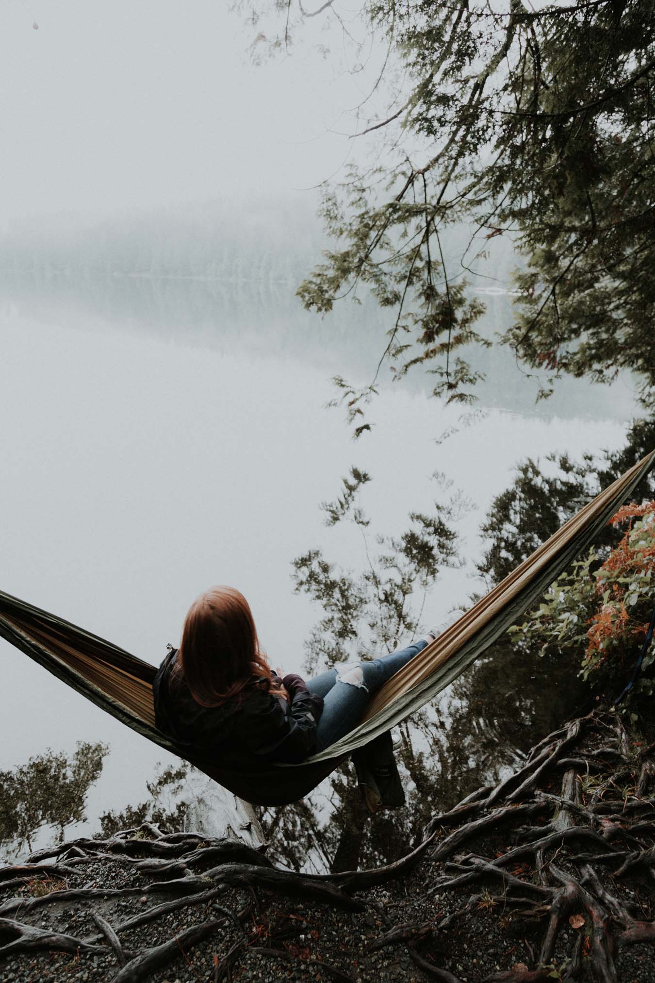 Young red-haired girl dangles her soul in a hammock by the lake