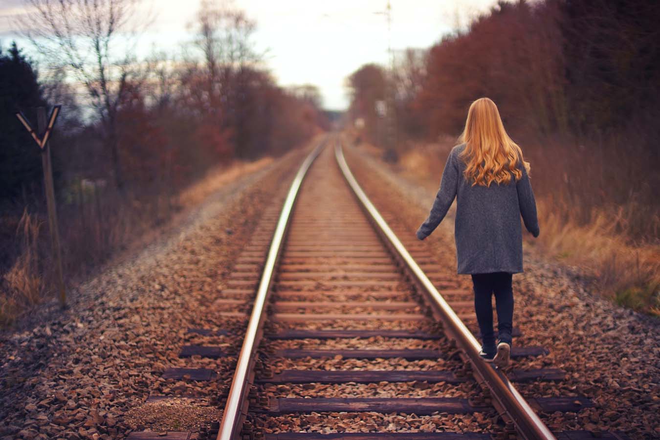 A young woman balances on a railroad track.