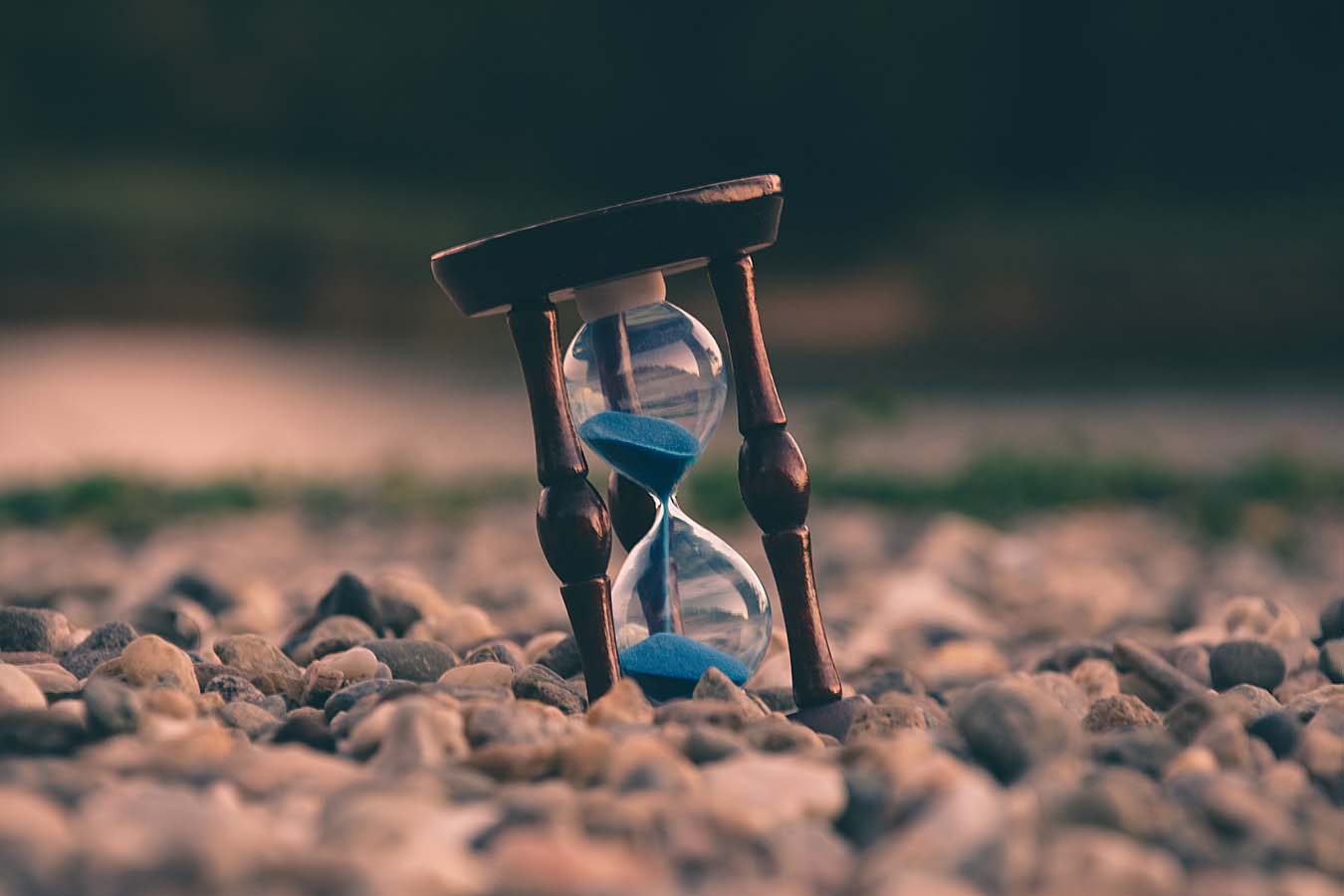 An hourglass with blue sand stands on a bed of stones.