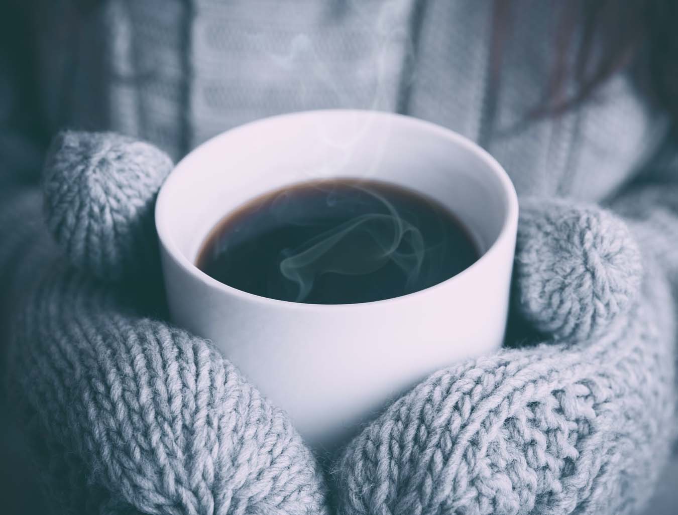 Hände in dicken Wollhandschuhen halten eine Tasse heißen Tee.