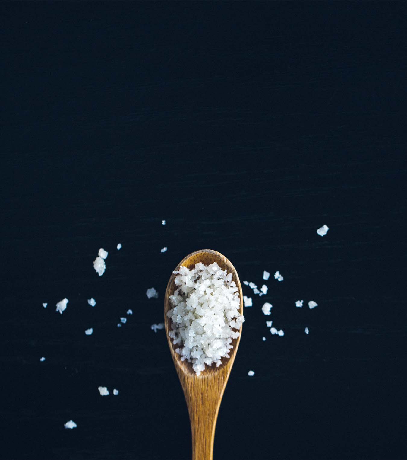 Rock salt on a wooden spoon placed on a black background.