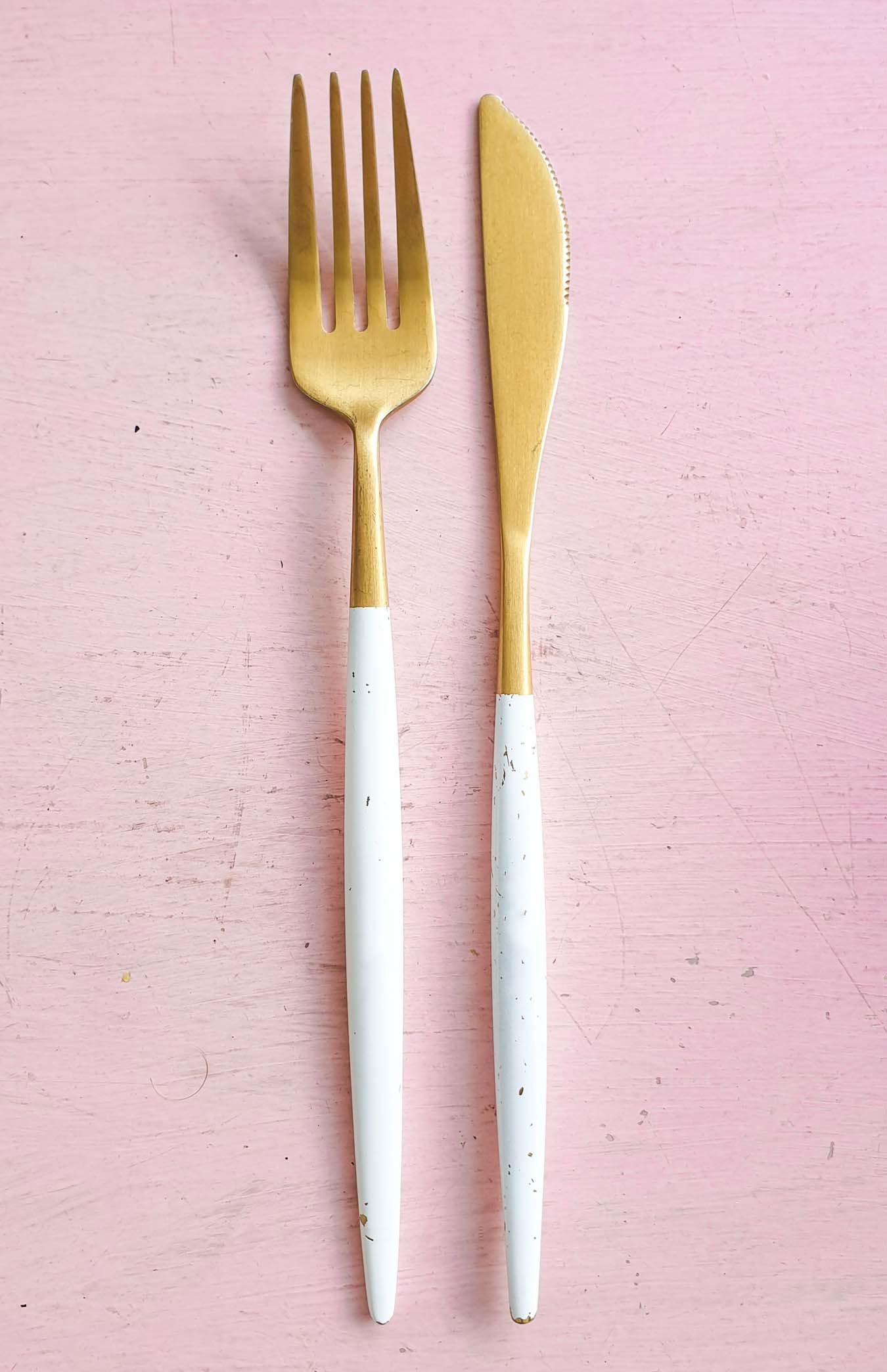 Golden fork and knife with a white handle on a rose background.