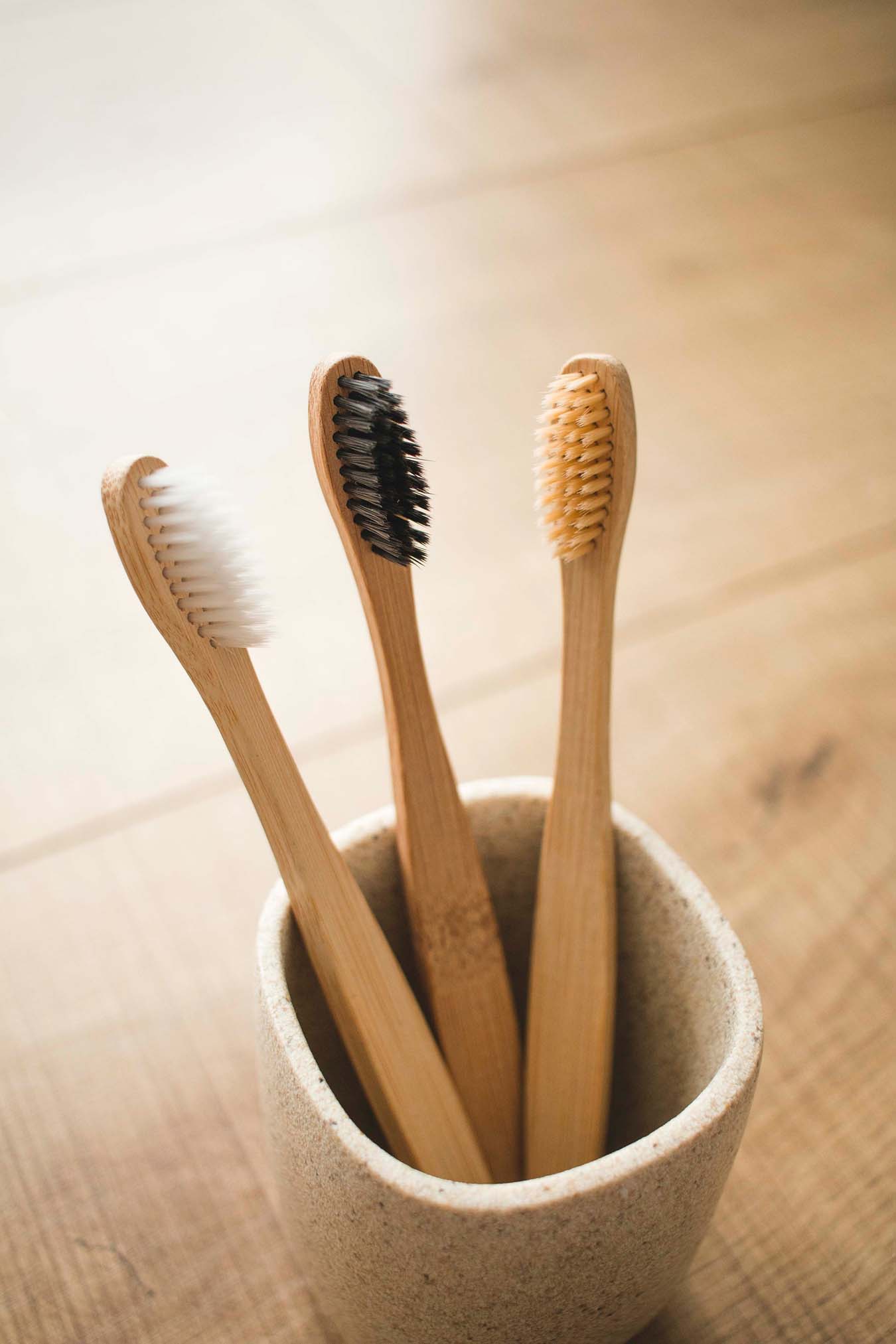 Three bamboo-toothbrushes stand in a gray ceramic bowl.