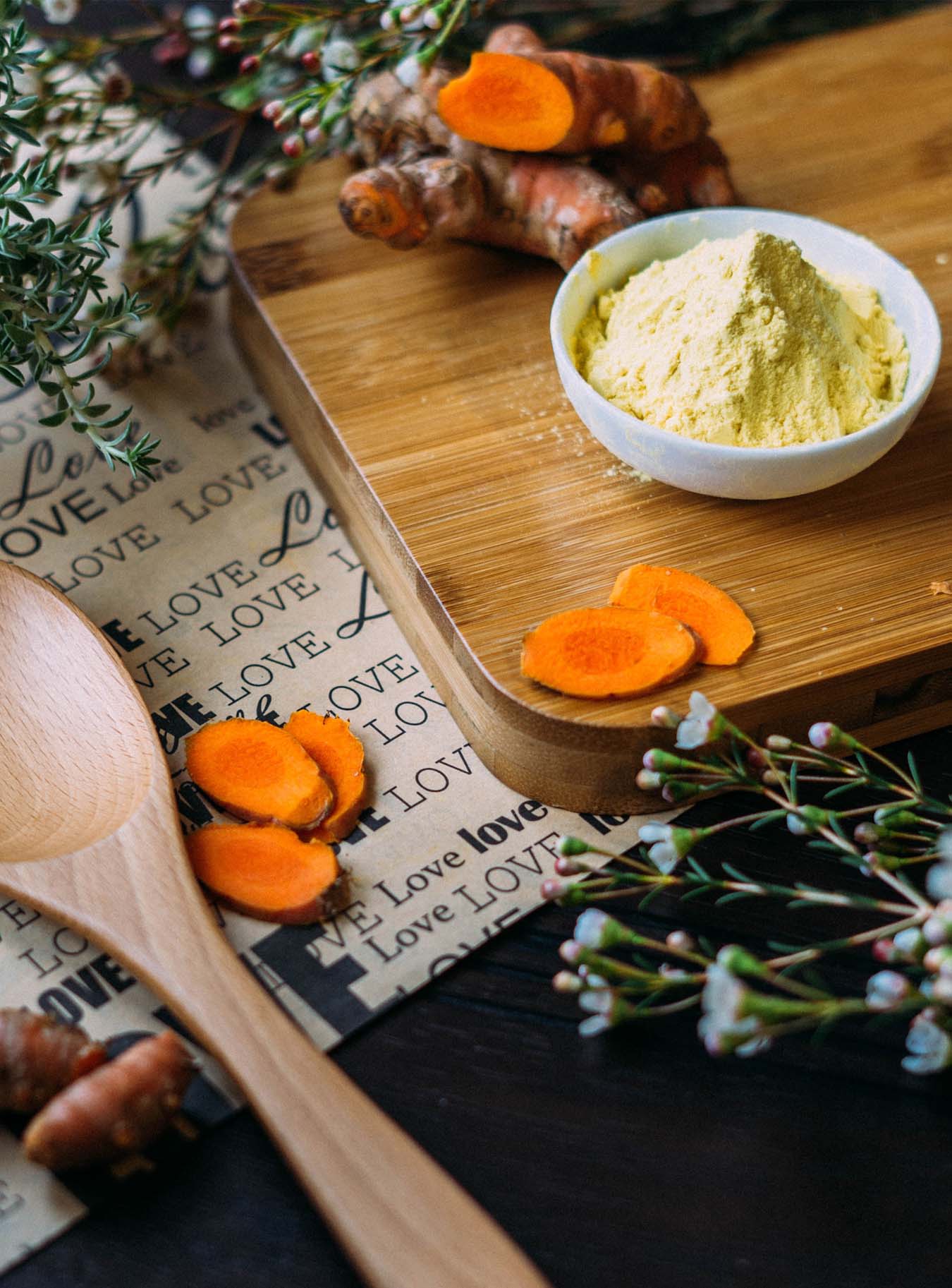 Yellow tumeric powder, a fresh tumeric root and some spices on a wooden board.