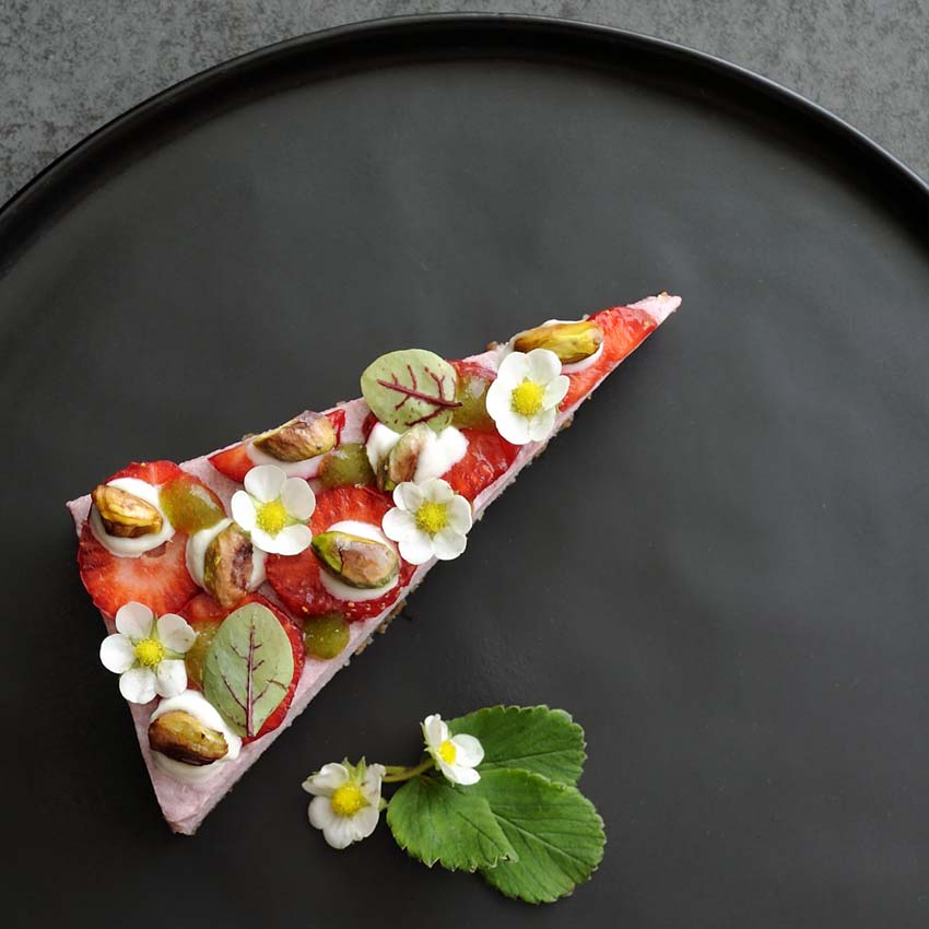 strawberry cake on black plate garnished with blood dock and strawberry flowers