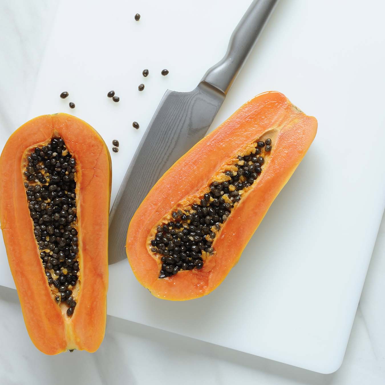 Aufgeschnittene Papaya auf weißem Brett - Messer daneben liegend