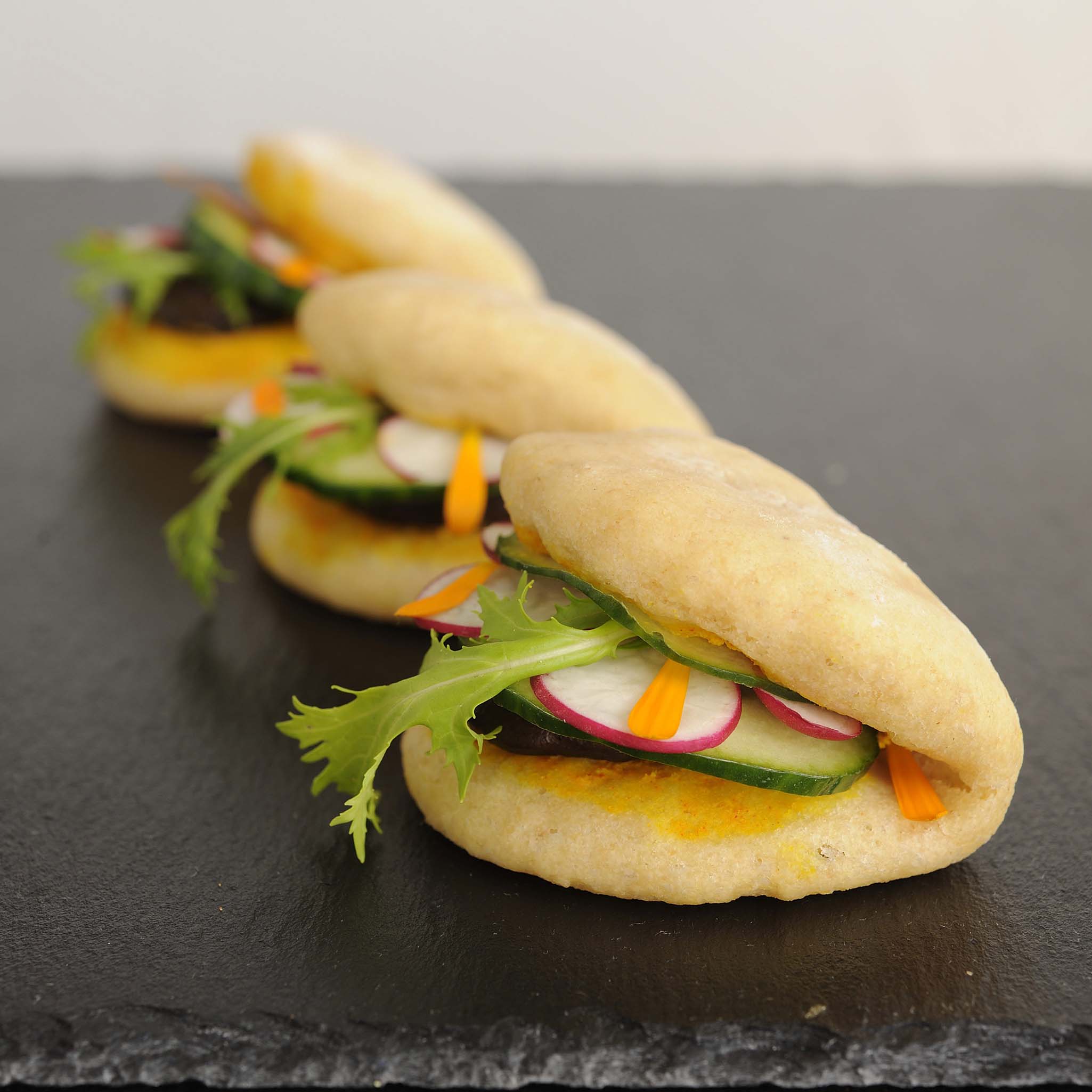 buns filled with arugula and radish on a black slate plate