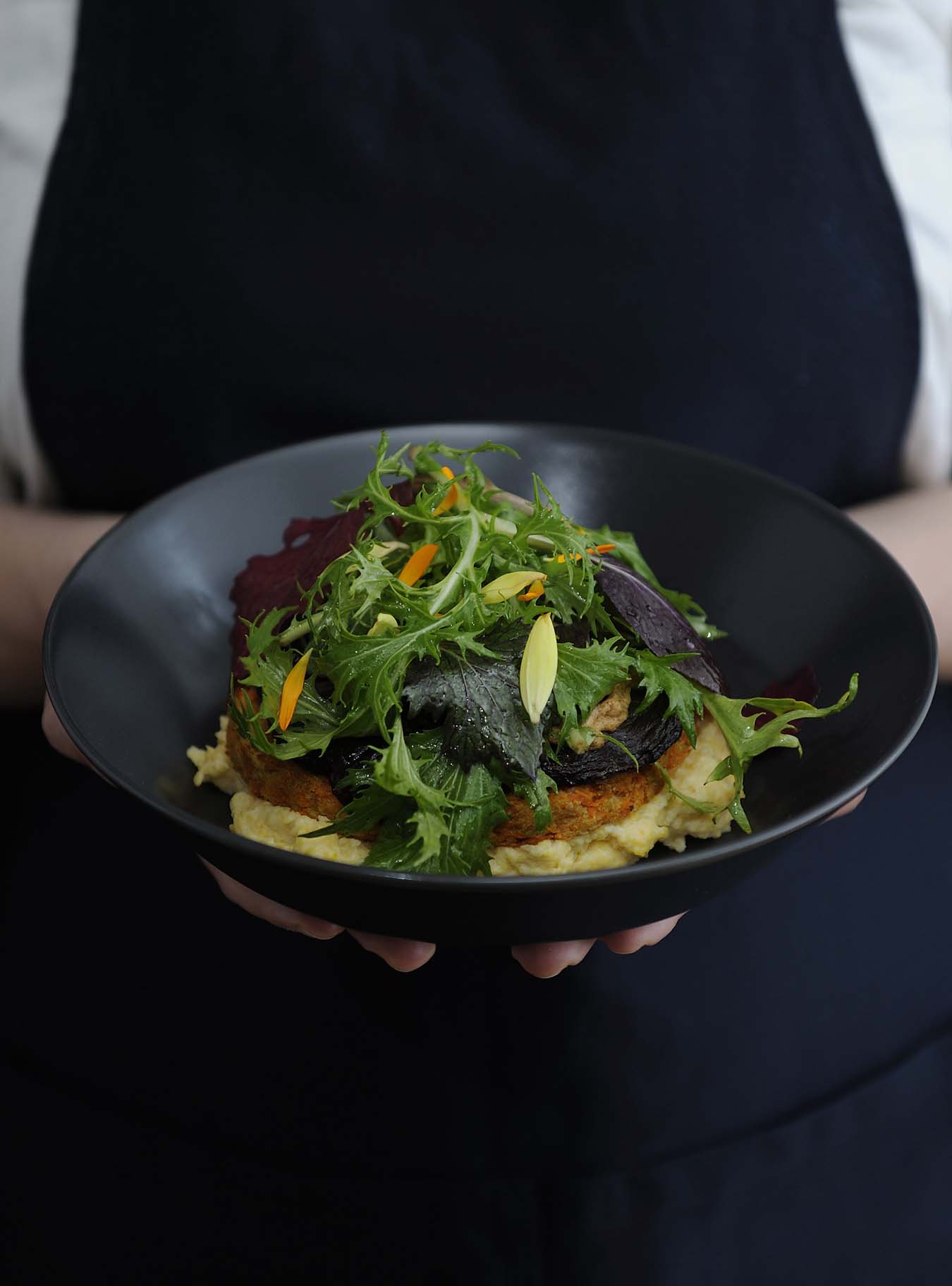 femlae hands holding a bowl with polenta - topped with shiitake mushrooms and salad