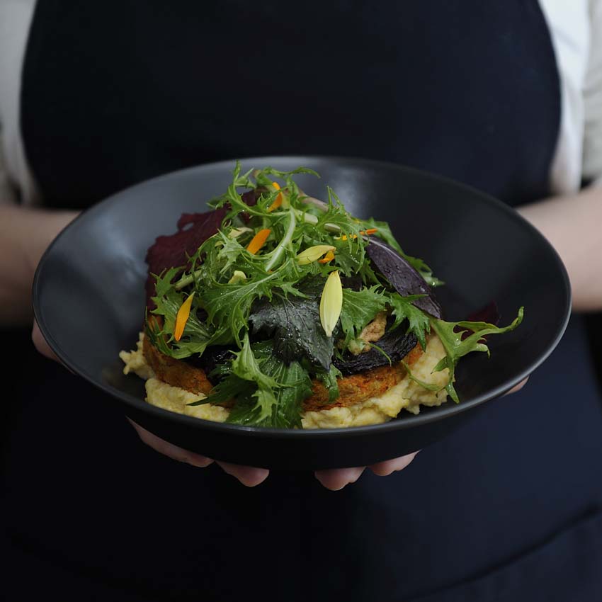 Frauenhände halten eine Schüssel mit Polenta - Shiitakepilze und Salat darüber