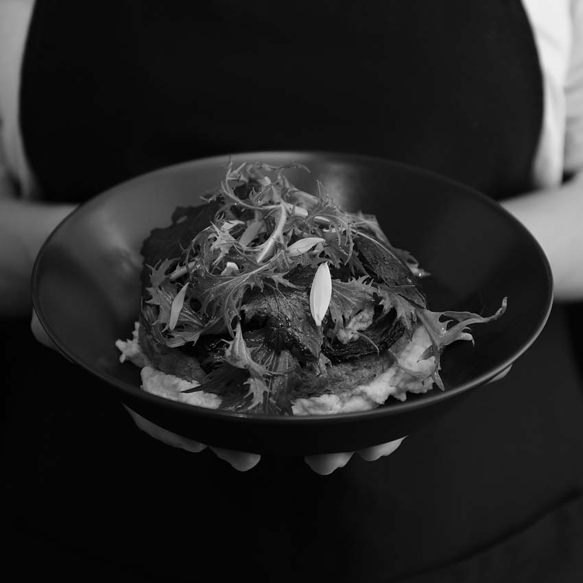 Frauenhände halten eine Schüssel mit Polenta - Shiitakepilze und Salat darüber