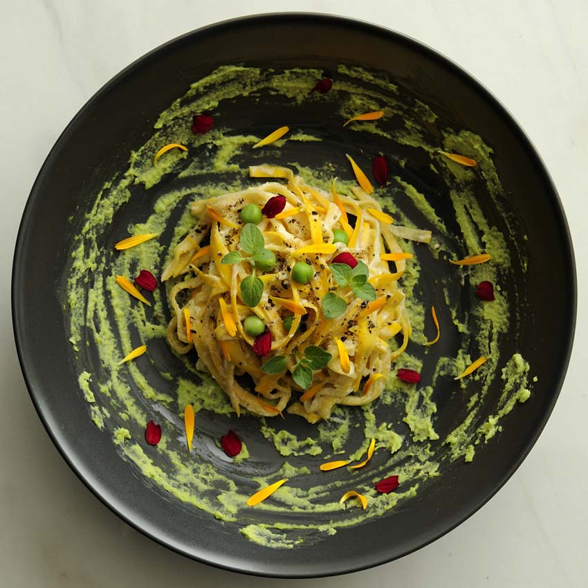 yellow summer squash noodles with green souce on black plate