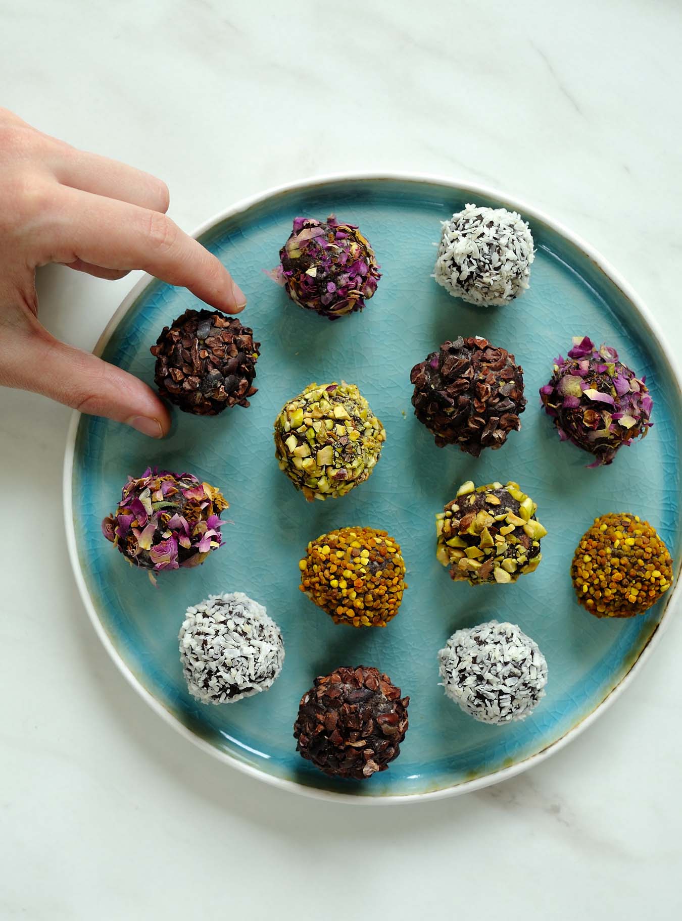 hand takes chocolate truffle from plate full of colorful truffles